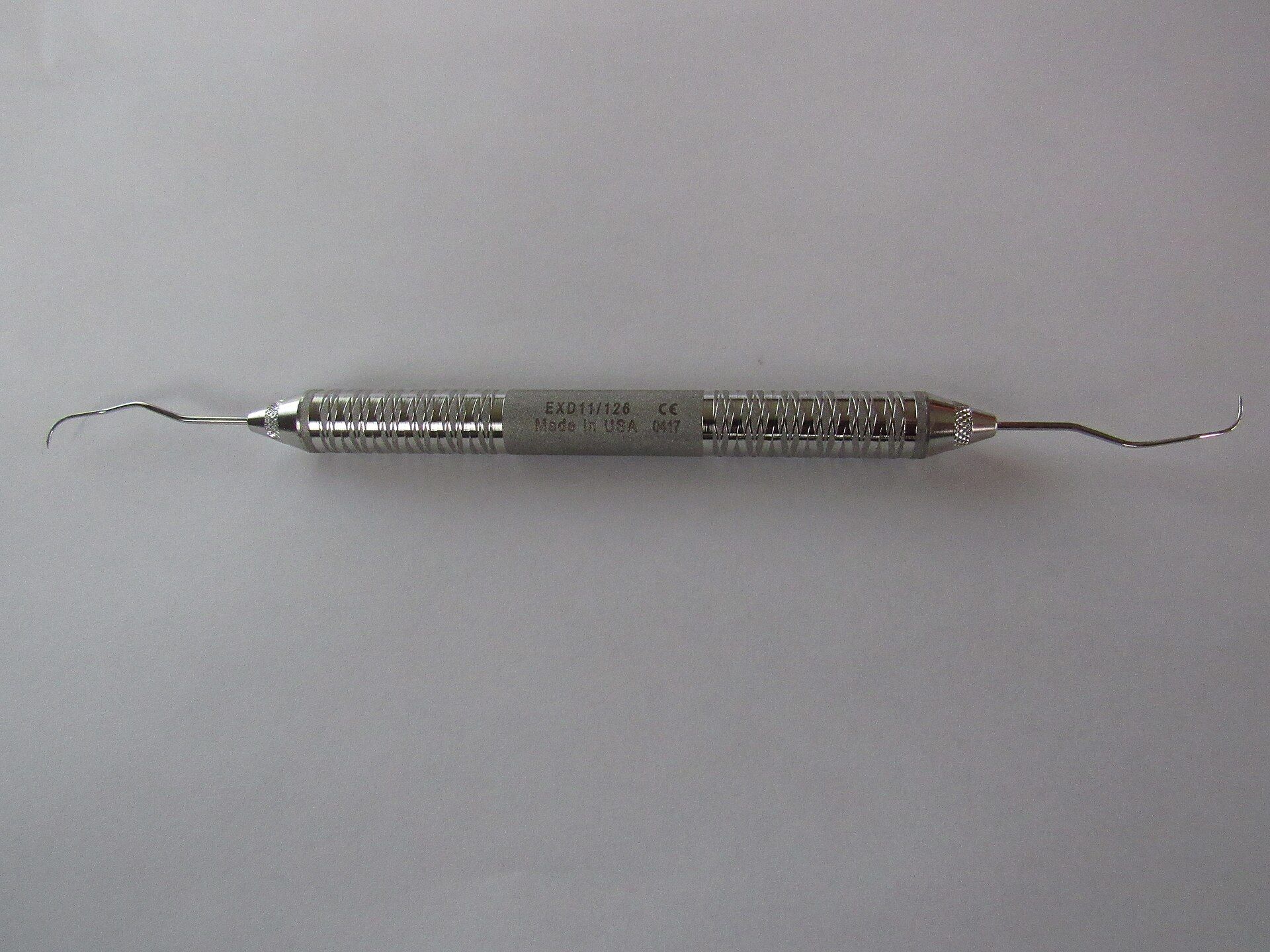 Instrumento dental de acero inoxidable sobre una superficie gris clara.