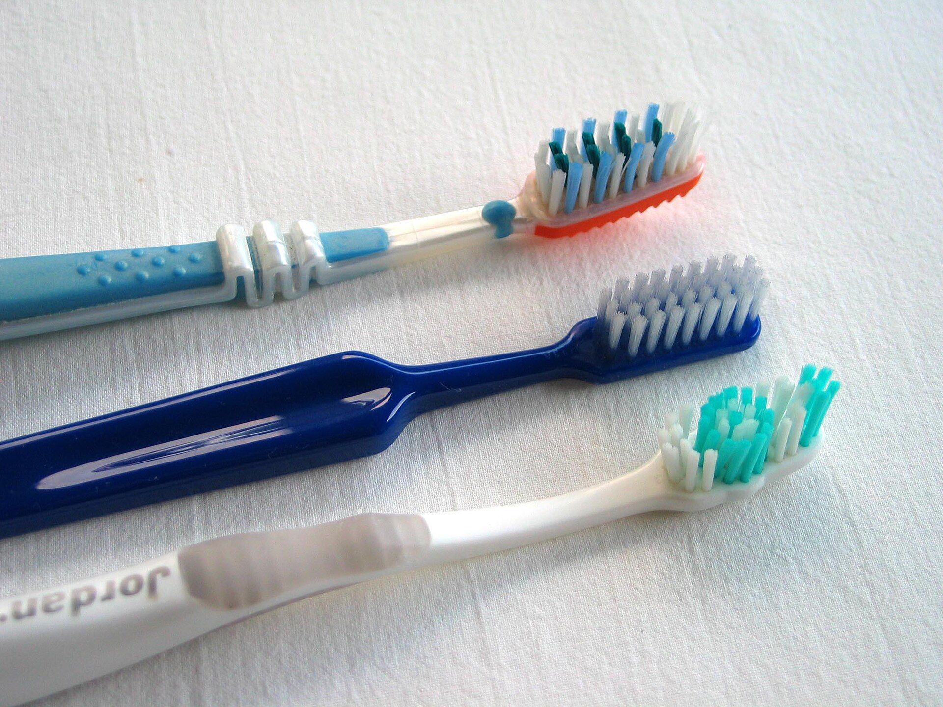 Tres cepillos de dientes de distintos colores sobre una tela blanca.